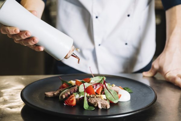 cook-pouring-sauce-plate-with-salad